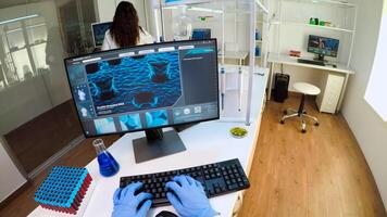 POV of researcher doctor typing at computer, analysing DNA scan image, while coworker bringing him samples of blood. Group of biochemistry scientists examining virus evolution using high tech photo