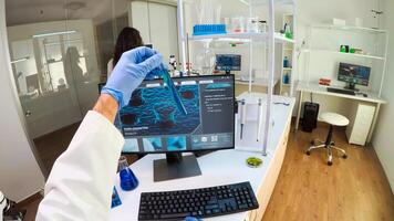 FPV of biologist doctor checking DNA image typing on pc, while colleague bringing tubes with samples, Scientists examining vaccine evolution in medical lab using high tech for scientific research. photo