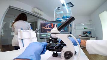 FPV of medical scientist looking under microscope, analyzes petri dish sample in equipped lab. Medical stuff examining vaccine development using high tech researching treatment against covid19 virus photo
