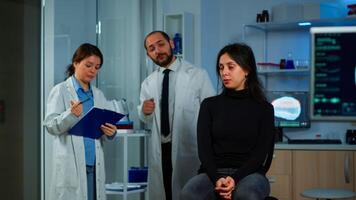 Woman waiting doctor sitting on chair in neurological research laboratory, while researchers team discussing in background health status of patient, brain functions, nervous system, tomography scan photo