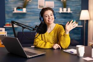 Social media influencer smiling at camera sitting in home studio ready for streaming new podcast. On-air online production internet broadcast show host streaming live content record digital blog. photo