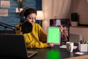 Influencer holding tablet with green screen display recording new podcast series for audience. Broadcast show host streaming live content for social media using mochup, chroma key, izolated desktop. photo