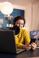 Blogger woman recording for her blog in home studio reading messages on smartphone. On-air online production internet broadcast show host streaming live content for social media. photo