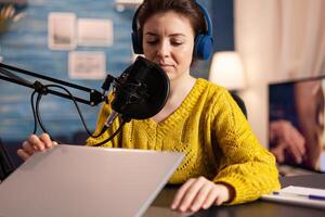 Famous blogger opening laptop and reading aloud in microphone recording podcast in modern studio creating content. On-air online production internet broadcast host streaming live show for social media. photo