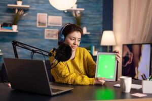 Blogger talking into microphone holding notepad with green screen during entertainment podcast. On-air production internet broadcast host streaming live content using chroma key, mockup display. photo