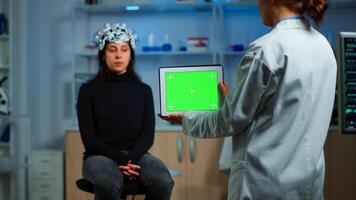 Neurologist doctor holding tablet with green screen in neurological research laboratory. Scientist using mockup chroma key display isolated desktop while patient with eeg headset wating in background photo
