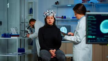 Researcher neurologist doctor asking patient's symptoms taking notes on tablet, adjusting high tech eeg headset. Doctor researcher controlling EEG headset analyzing brain functions and health status photo