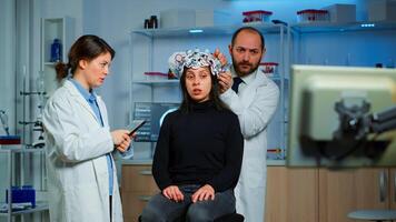 Professional neurological researcher explaning treatment result pointing on monitor while medical scientist adjusting eeg headset preparing for brain scan analysing electrical activity, nervous system photo