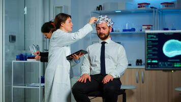 Man with brainwave scanning headset visiting professional doctor treating nervous system dysfunctions. Patient sitting in brain study laboratory while neurologist scientist adjusting eeg device photo
