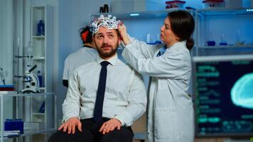 Woman researcher putting brainwave scanning headset to patient developing experiments using brain study lab monitors. Man siting on chair while scientist adjusting device examining nervous system photo