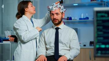 Patient with brainwave scanning headset sitting in brain study laboratory while neurologist scientist adjusting high tech device. Man visiting professional doctor treating nervous system dysfunctions photo
