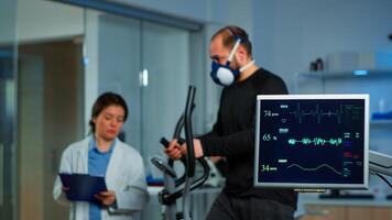 Team of medial researchers monitoring vo2 of man performance sports wearing mask running. Lab science doctor measuring endurance of sportsman while ekg scan runs on computer screen in laboratory photo