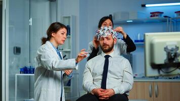 Neurological researchers explaning treatment result pointing on monitor while medical scientist adjusting brainwave scanning headset preparing for brain scan analysing electrical activity photo