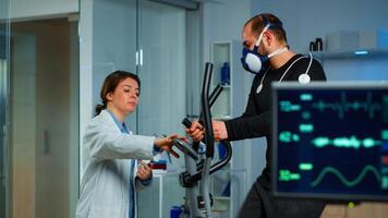 Specialist health supervisor increasing level of exercises monitoring endurance of athlete. Medical researcher measuring vo2 of performance sports running with mask on cross trainer in sport lab photo