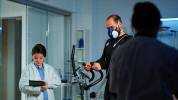 Patient making electrocardiogram during physical exercise in sports science lab, monitoring endurance and heart rate, computer showing EKG data on display. Man running with mask and medical electrodes photo