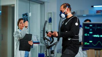 Medical doctors in sports science lab measuring performance cardiorespiratory of athlete. Team of researcher monitoring vo2 of sportsman running on cross trainer equipped with electrodes and mask photo