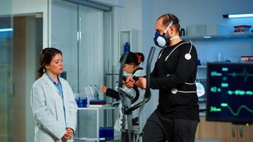 Sportsman running on cross trainer in lab facility for sports performance, medical researcher monitoring endurance and heart rate. Monitor showing EEG, EKG reading of athlete running on cross trainer photo