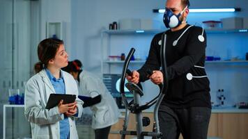 Medical researcher talking with sportsman while measuring his endurance using body sensors, electrodes and mask monitoring cardiac rhythm. Patient running on cross trainer in sports science lab photo