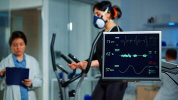 Monitor showing EKG scan of athlete running on cross trainer and medical specialists supervise exercise in background, controlling physical activity, measuring heart rate in sports science laboratory photo