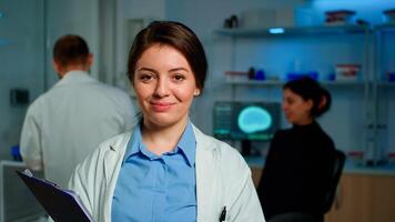 Close up of medical neurologist researcher smiling at camera standing in lab holding clipdoard while coworker discussing with patient about brain health care, nervous system, tomography scan photo