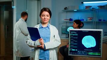 Portrait of medical neurologist researcher looking at camera smiling holding clipdoard while coworker discussing with patient about brain health care, nervous system, tomography scan working in lab photo