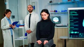 Team of scientists specializing in neurological medicine discussing health status of patient, brain functions, nervous system, tomography scan while woman waiting diagnosis of disease sitting in lab photo