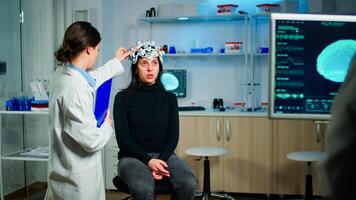 Stressed patient sitting on neurological chair with eeg headset, testing health status of brain, while medical researcher looking at monitor with tomography scan developing treatment in laboratory photo