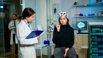 Medical doctor and patient discussing about symptoms of disease during eeg scan using high tech headset in lab. Analysing health status of woman, brain functions, nervous system, digital tomography photo