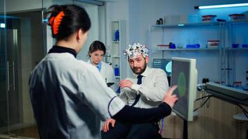 Medical doctor pointing on computer monitor with touch screen testing physical reactions and nervous system of man wearing brainwave scanning headset in technologically advanced laboratory photo
