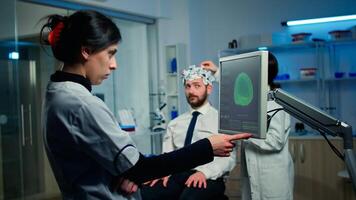 Woman researcher looking at monitor analysing brain scan while coworker discussing with patient in background about side effects, mind functions, nervous system, tomography scan working in laboratory photo