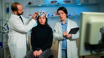 Woman doctor explaning tomography scan from monitor computer while man researcher adjusting eeg headset monitoring brain reactions. Examining evolution of treatment against diseases in equipped lab photo