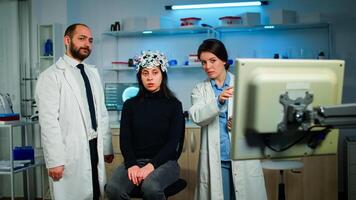 Team of medical researchers testing nervous system of woman patient, looking together at brain scan on computer monitor. Doctors examining evolution of treatment against diseases in equipped lab photo