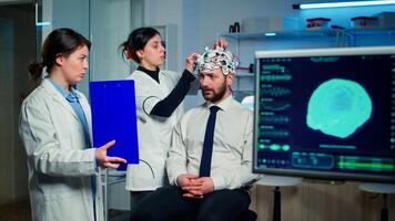 Professional doctor in neurological medicine pointing on clipboard testing eyesight of man with eeg headset. Medical reasearcher examining evolution of treatment against diseases of nervous system photo