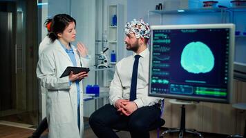 Specialist doctor in neuroscience taking notes on clipboard while testing brain functions of man using eeg headset, treating nervous system dysfunctions in moden laboratory. photo