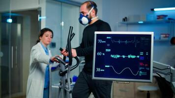 Monitor shows EKG reading of man athlete running on cross trainer and discussing with medical reseacher. Specialist supervising exercise process, controlling physical activity and muscular endurance photo