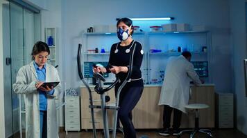 Team of medial researchers monitoring vo2 of woman performance sports wearing mask running. Lab science doctor measuring endurance using tablet while ekg scan runs on computer screen in laboratory photo