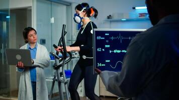 Doctor scientist holding laptop computer and controling EKG data showing on laboratory monitors. Lab science researcher measuring endurance of athlete, heart rate using electrodes and mask photo