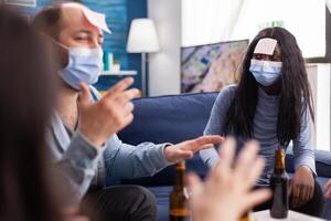 African woman with sticky note on forehead playing name game with cheerful happy friends wearing face mask to prevent infection with covid19 due to social pandemic. Beer bottle, photo