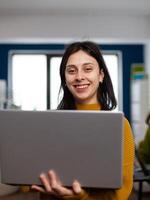 Woman designer creator looking at camera smiling while working in design post production agency. Videographer graphic editor standing in multimedia company holding laptop editing creative photo