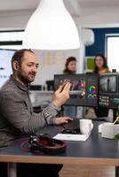 editor discussing online with customer designer holding smartphone editing footage sitting in multimedia company. Man creator artist processing movie montage using post production software photo