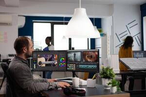 editor cuting footage working at film editing montage on computer with dual monitors setup in multimedia creative agency office. Videographer man processing film using post production software photo