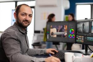 Creative designer artist man looking at camera smiling working in creativity multimedia startup office using editing post production software on professional pc. Processing film montage. photo
