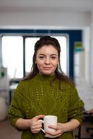 Portrait of designer artist smiling at camera holding cup of coffee standing in start up multimedia agency office. Woman working in creativity studio production editing design with diverse team. photo
