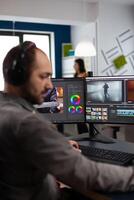 maker with headset working with footage and sound on pc with two displays, taking notes while editing customer creative . Man editor processing film montage in startup agency office. photo