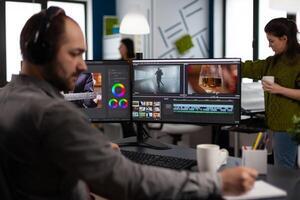 maker with headset working with footage and sound on pc with two displays, taking notes while editing customer creative . Man editor processing film montage in startup agency office. photo