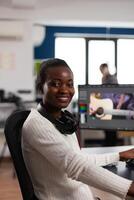 African american editor artist looking at camera smiling editing creative project in post production software working in startup studio office. Videographer editing audio film montage photo