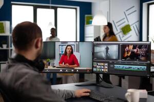 editor in web online production conference with project manager on call editing client work, getting feedback on company movie using post production software on two monitors photo