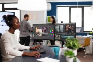 African american editor wearing headset editing movie using post production software working in start up company office. Black creator processing footage on computer with dual displays photo