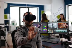 editor experiencing virtual reality headset, gesturing, editing film montage using post production software working in creative company office. Videographer using VR headset in multimedia agency photo