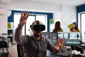 editor experiencing virtual reality headset, gesturing, editing film montage using post production software working in creative company office. Videographer using VR headset in multimedia agency photo